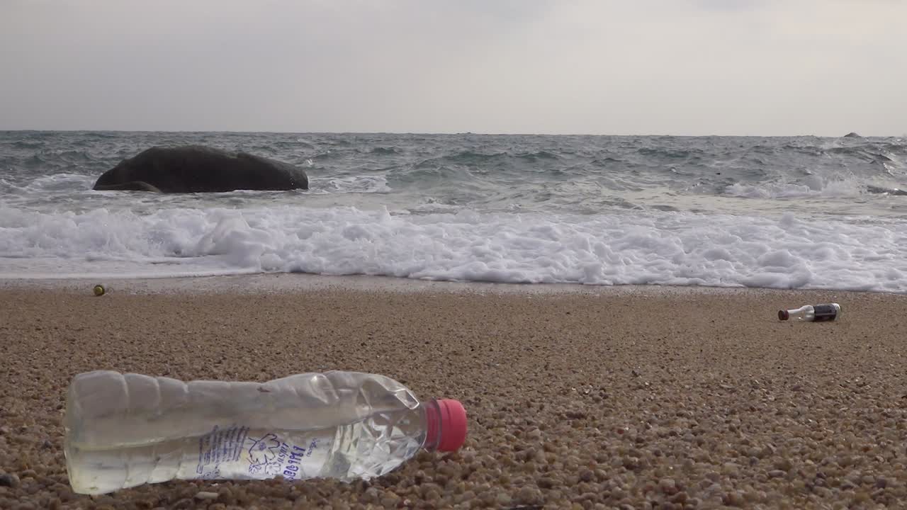 una botella de plástico ensuciada dejada en la playa lavada por las olas, toma estable y estable