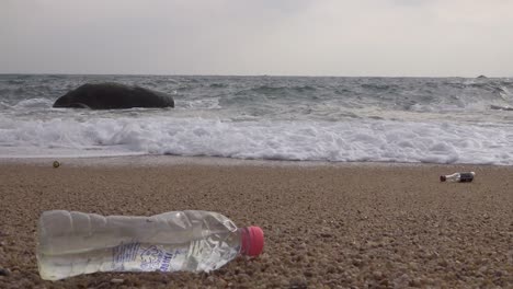 Una-Botella-De-Plástico-Ensuciada-Dejada-En-La-Playa-Lavada-Por-Las-Olas,-Toma-Estable-Y-Estable