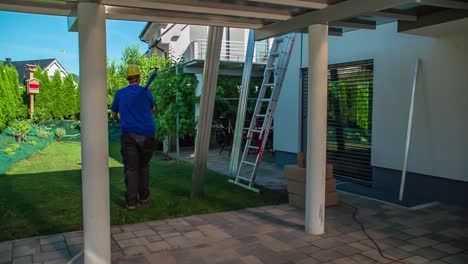 Roofer-Carrying-Solar-Panel-Rails-On-Shoulder-To-Be-Placed-Next-To-Ladder