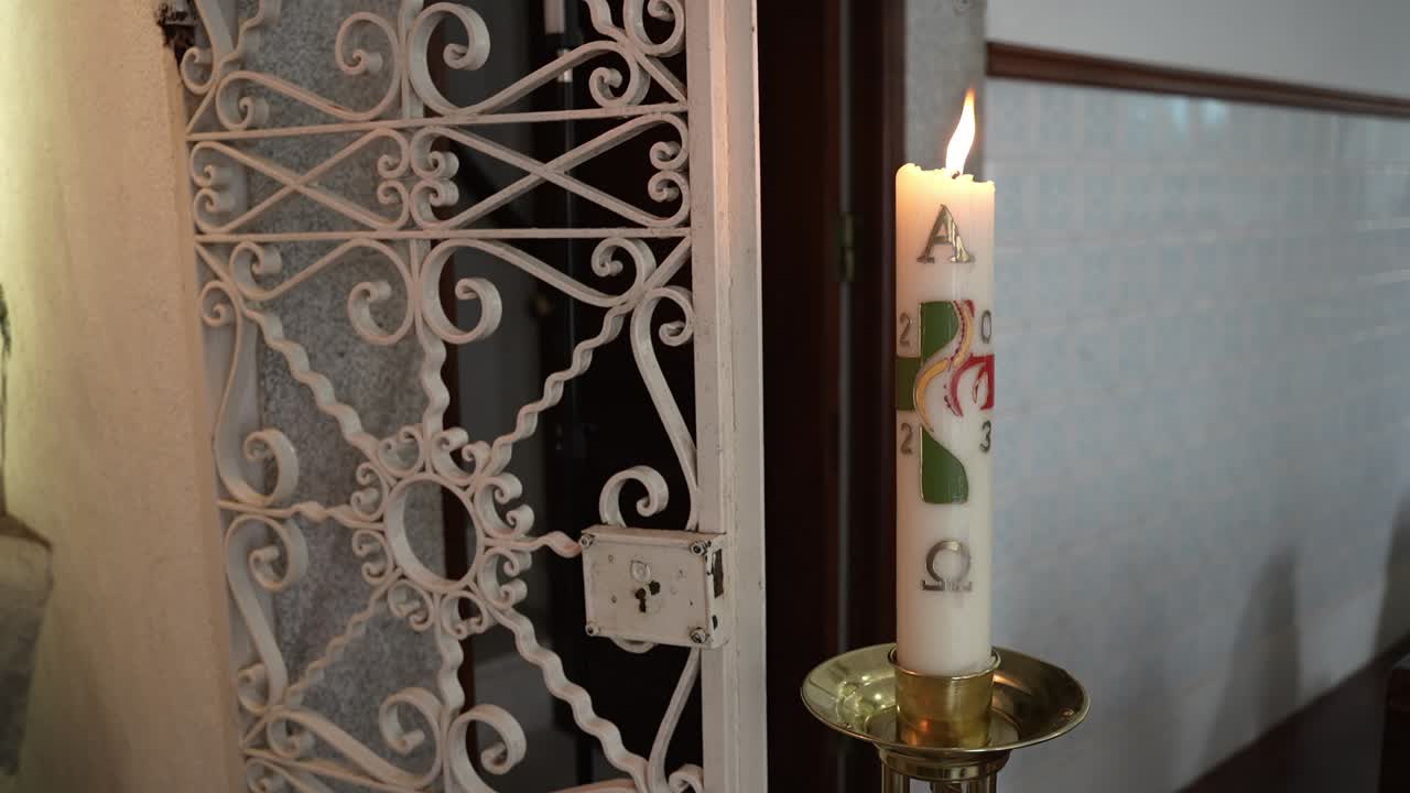 vela pascual decorada ardiendo junto a una rejilla metálica adornada dentro de la iglesia