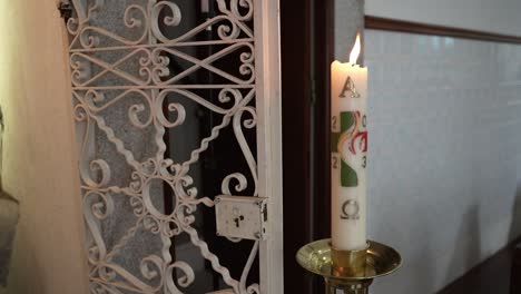 vela pascual decorada ardiendo junto a una rejilla metálica adornada dentro de la iglesia