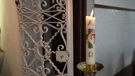 decorated paschal candle burning beside ornate metal grille inside church