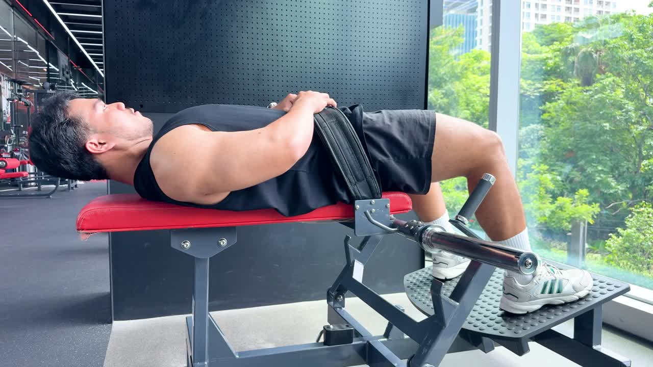 Athletic man uses leg press machine in bright gym with large windows and city view