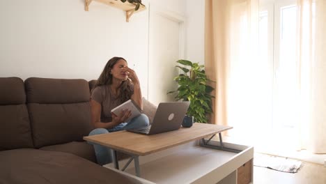 stressed woman writing in notebook while working on laptop at home