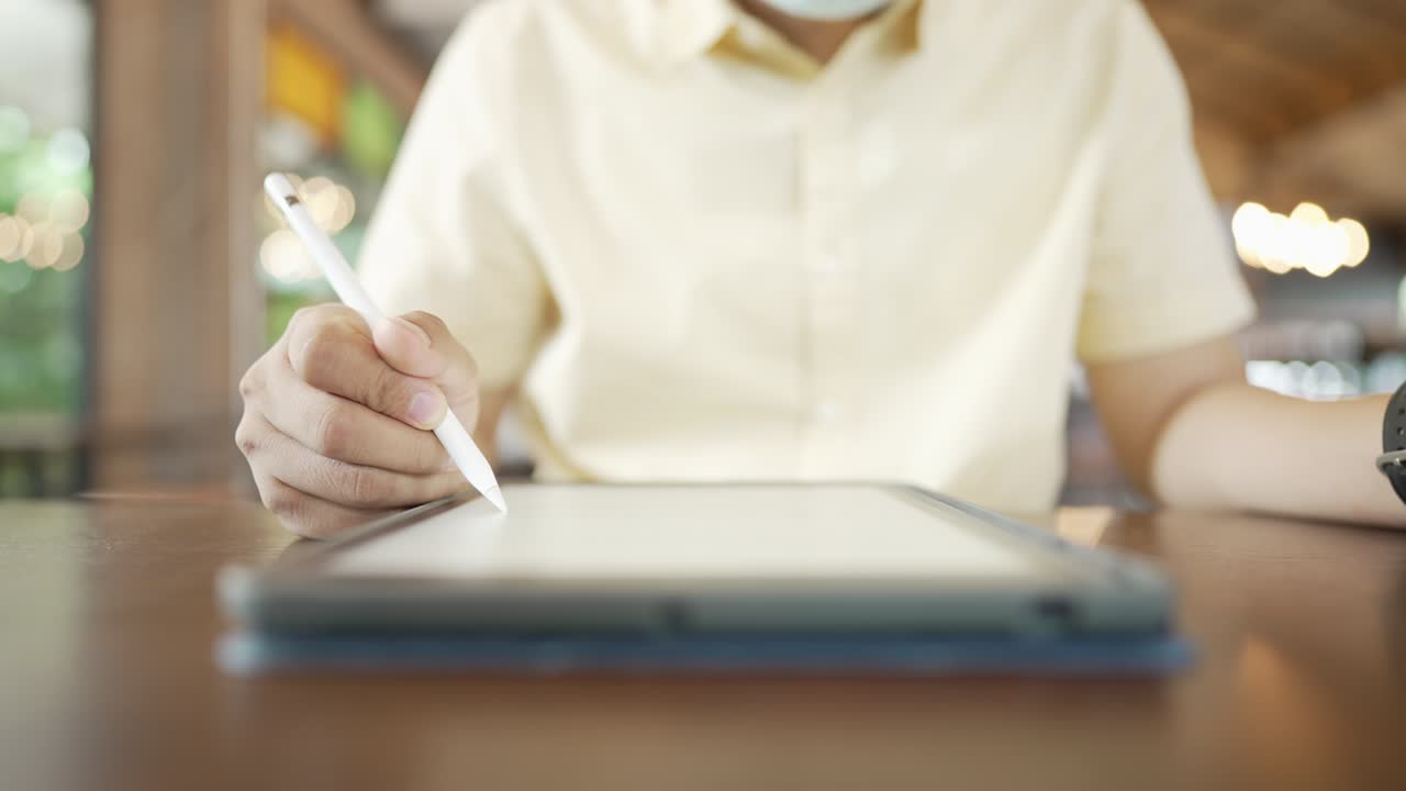 A young businessman wearing a surgical mask is doing a video conference with customers via a tablet that is connected to the Internet
