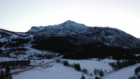 Casas-De-Ocio-En-La-Ladera-De-La-Montaña-Cerca-De-La-Estación-De-Esquí-En-Hemsedal-Noruega---Antena-Oscura-Tarde-En-La-Noche-En-El-Famoso-Destino-De-Esquí-Con-Fondo-De-Cielo-Brillante-Detrás-De-La-Montaña-Rogjin