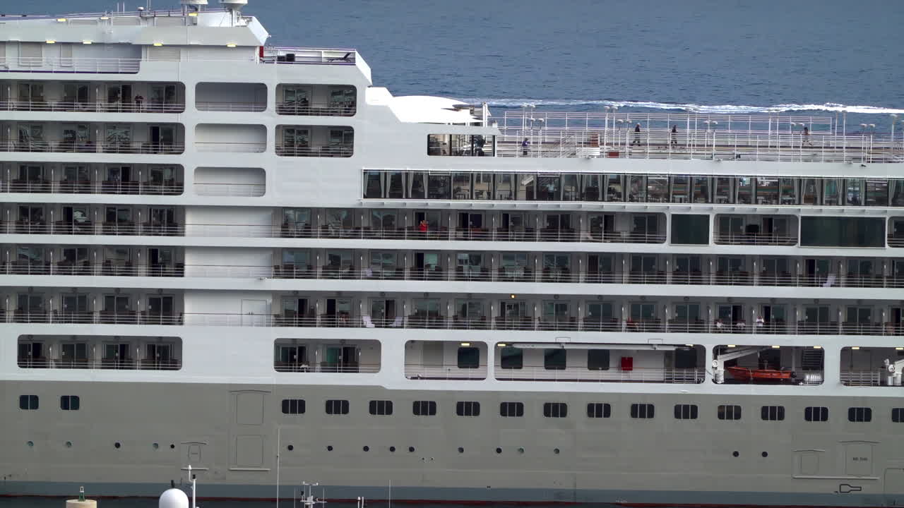 La Condamine, Monaco - July 4, 2025: Side view of a large cruise ship docked in Monaco, revealing multiple decks, balconies, and passengers enjoying ocean view