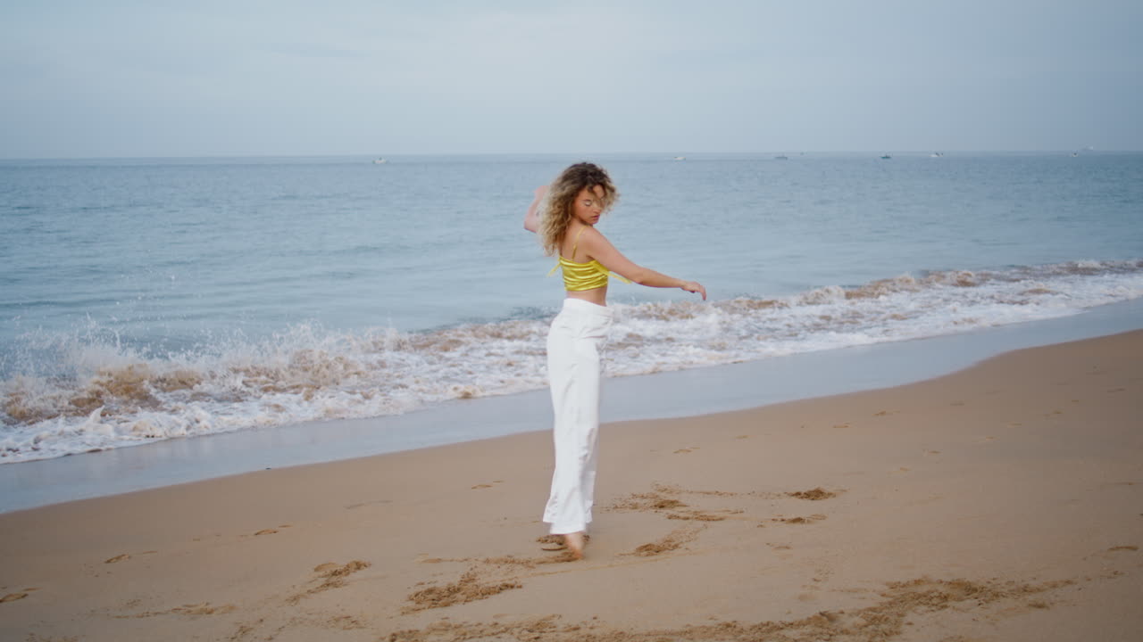 바다의 파도에서 현대적인 안무 연습을 하는 댄서. 곱슬한 여자 춤