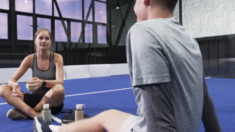 smiling female athlete rolling tennis ball under foot explaining recovery tips to friend on court
