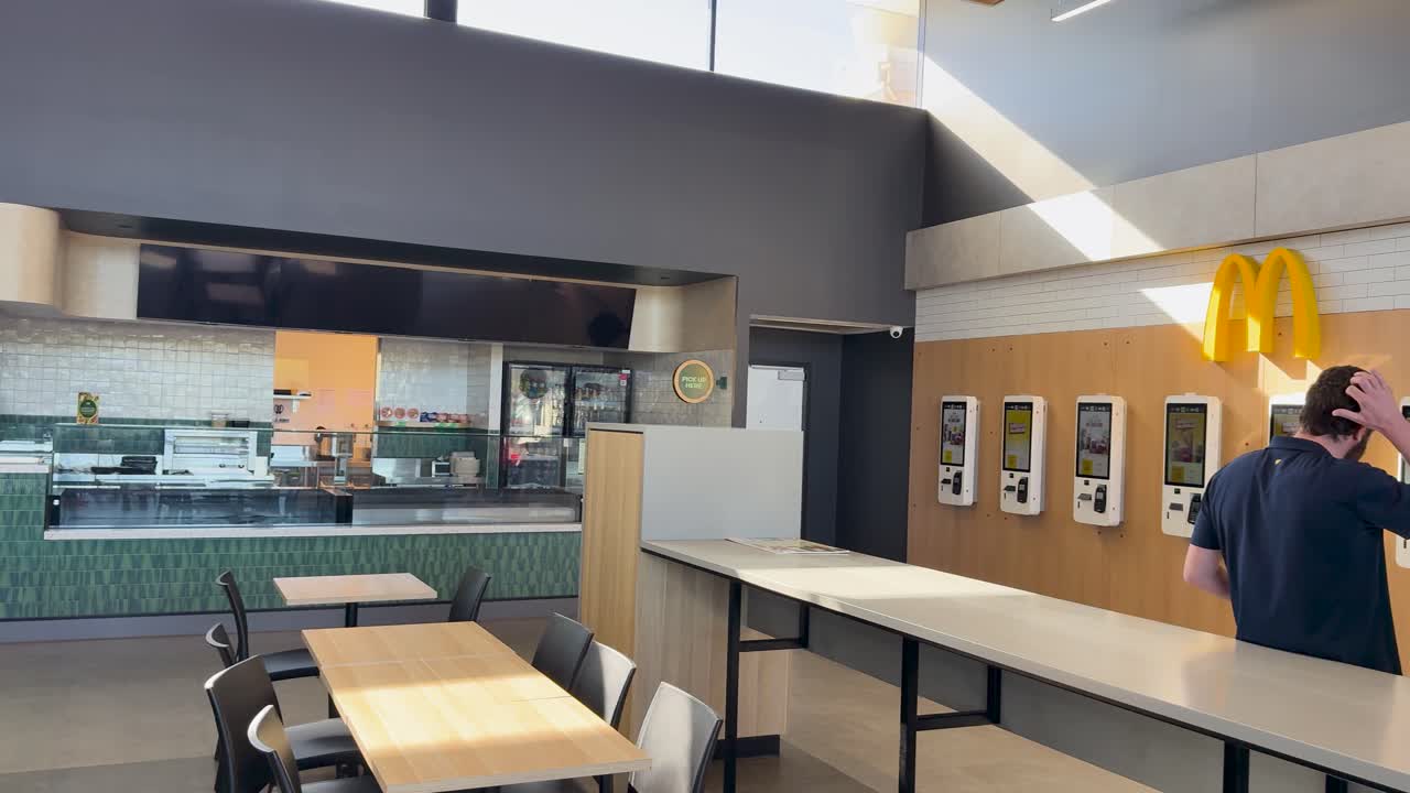 Individuals walk through a modern rest stop food court with multiple dining options visible
