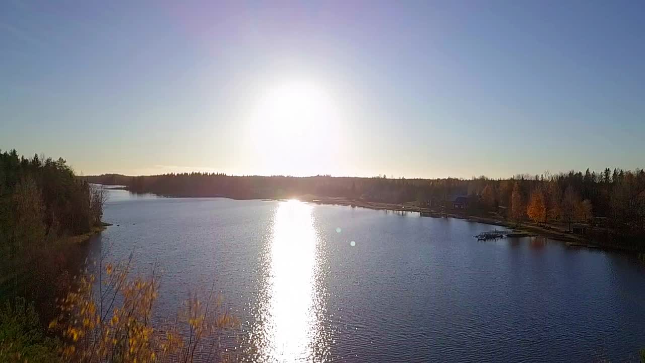Aerial ascending close to trees revealing idyllic rural lake village lit up by autumn sunset, Ostrobothnia, Finland