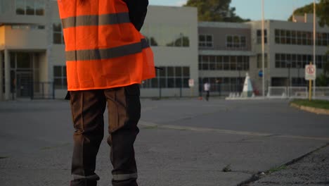 cropped image of a security personnel in orange hi-vis watching a kid playing football outdoor