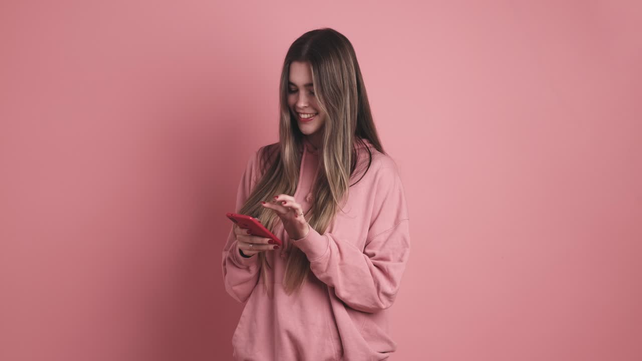 Счастливая молодая женщина стоит и набирает сообщение на смартфоне.