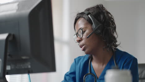 asistente médica africana usa casco blanco auriculares llamando a un paciente distante por computadora. médico hablando con el cliente usando una aplicación de computadora de chat virtual. telemedicina atención médica remota