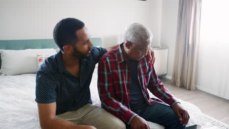 adult son comforting senior father suffering with depression at home