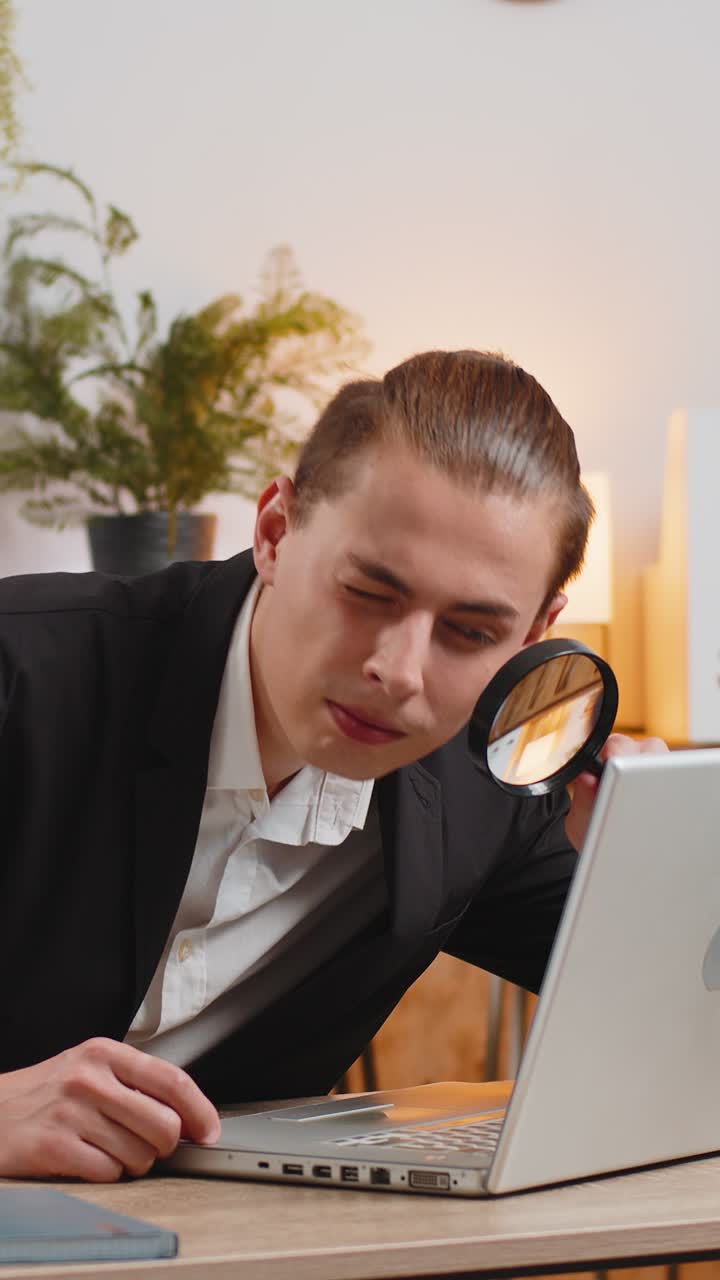 удивленный исследователь бизнесмен работает в домашнем офисе с увеличительным стеклом смотрит на ноутбук