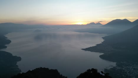 drone view in guatemala flying back from a blue lake surrounded by green mountains and volcanos on a cloudy day in atitlan