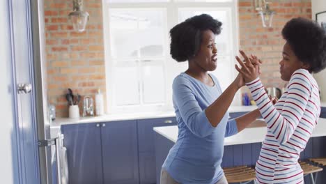 Happy-african-american-mother-and-daughter-dancing-together-in-kitchen