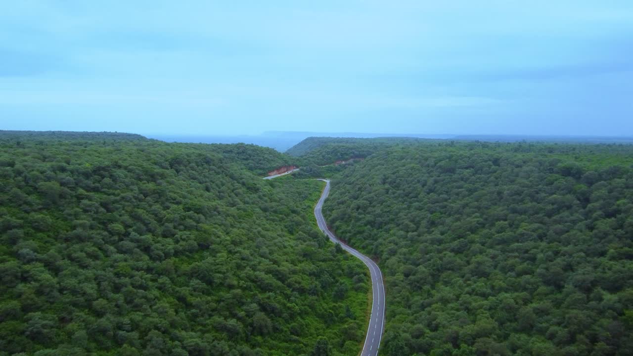 vista aérea de un avión no tripulado de una motocicleta en una carretera forestal a través de una selva verde exuberante con un telón de fondo montañoso durante el monzón en gwalior madhya pradesh india