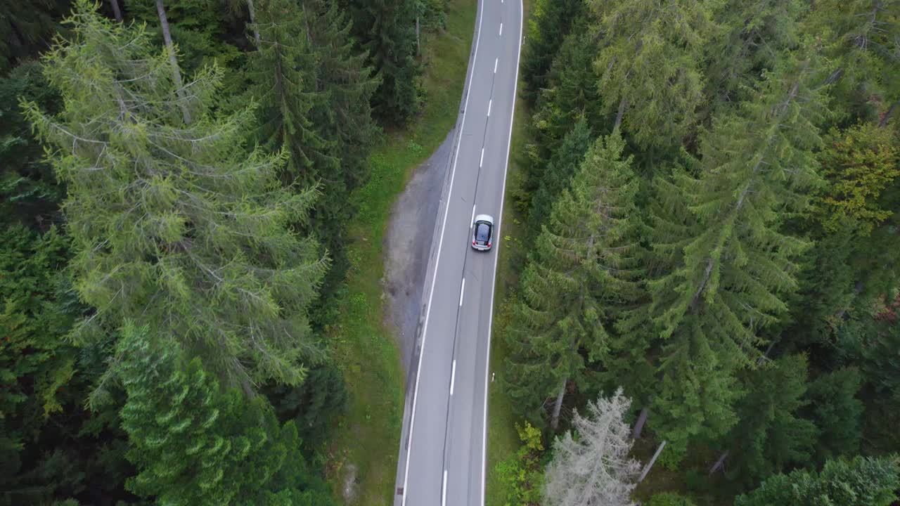Vista aerea da drone che sorvola un'auto elettrica su una strada, nei boschi della Svizzera