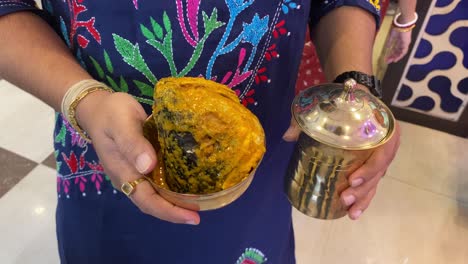 In-a-Bengali-ritual-in-Kolkata,-a-guy-is-shown-carrying-the-fish's-head-beside-a-golden-colored-copper-glass-with-a-cover