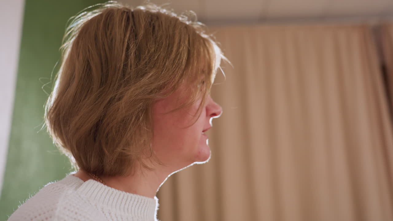 Side view of patient seated indoors engaging in calm conversation during therapy session, wearing white knit sweater, captured in soft lighting against muted background