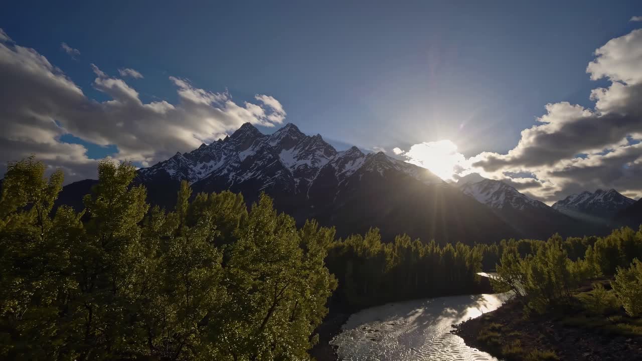 Aerial video captures a serene river winding through lush forests with sunlit mountains