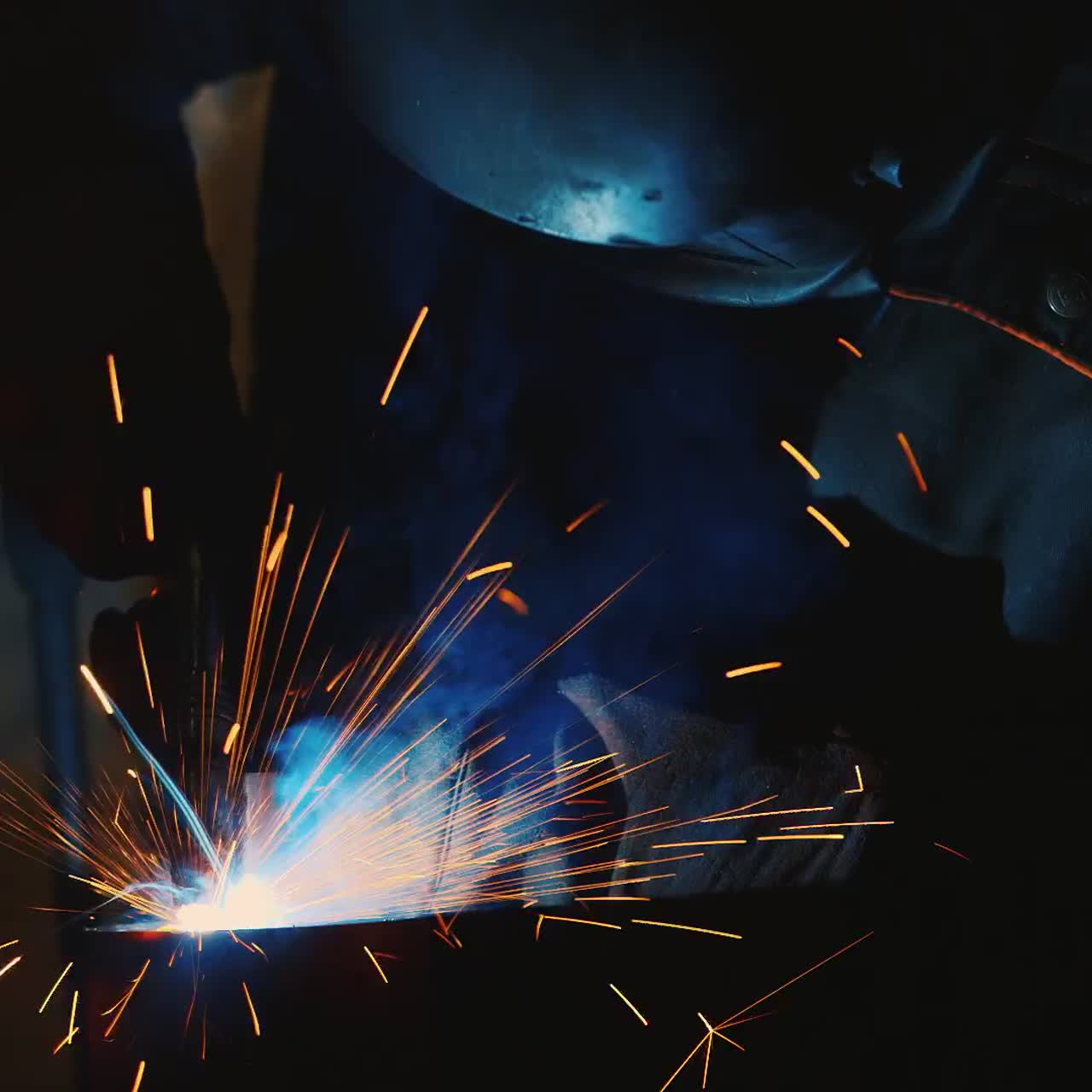 A welder in a protective helmet and clothes welds as sparks fly 4