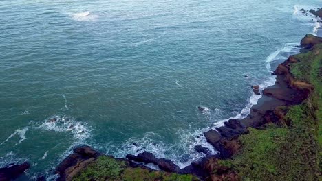 Rising-aerial-view-of-waves-crashing-on-beach-cliffs-on-California-coast