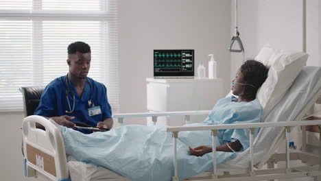 a male doctor is talking to a patient lying on a hospital bed in a hospital ward. connected to oxygen and a mask.