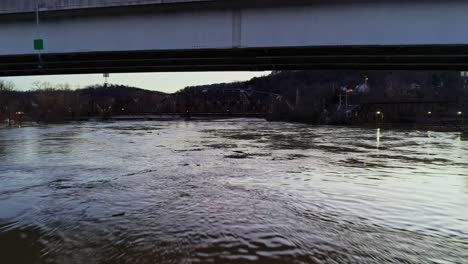 drone flying under bridge as car crosses over a river at sunset during a cold winter