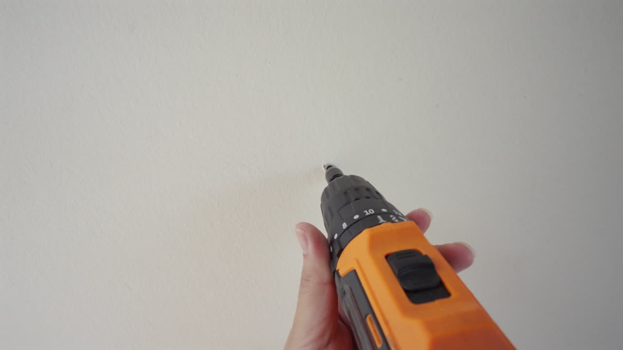 Female hands drive a wall screw with a cordless screwdriver using smooth steady motion indoors