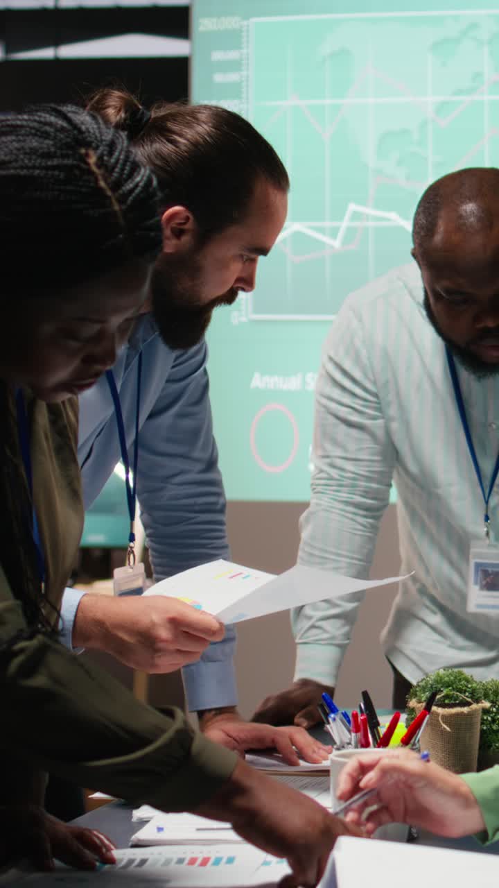 Vertical Video Multiethnic team exchanging files and review forecasting diagrams at night