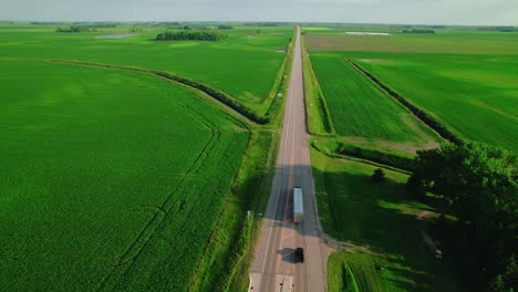 aerial view following a dry van trailer driving on a rural highway through agricultural fields