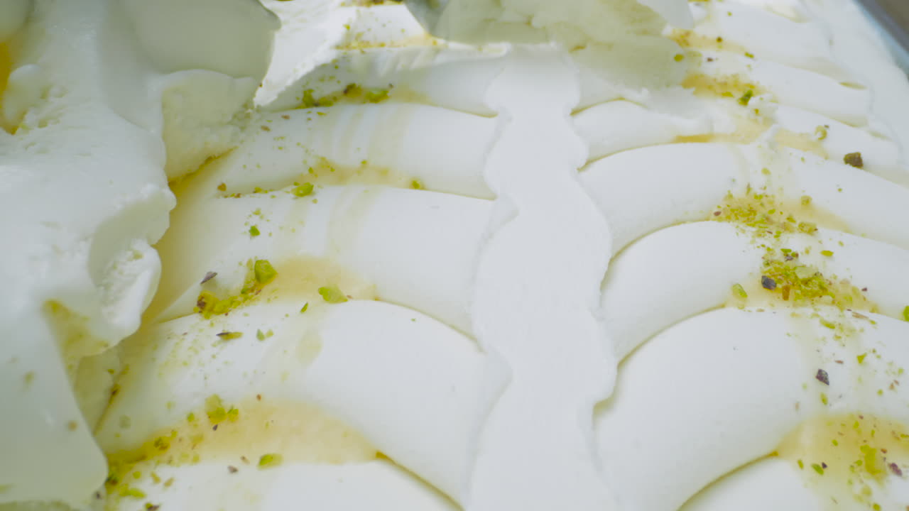A close-up of a creamy mascarpone ice cream with pistachio chunks, served with a metal scoop. The smooth texture, color contrasts, and crunchy topping create a delicious and visually appealing scene.