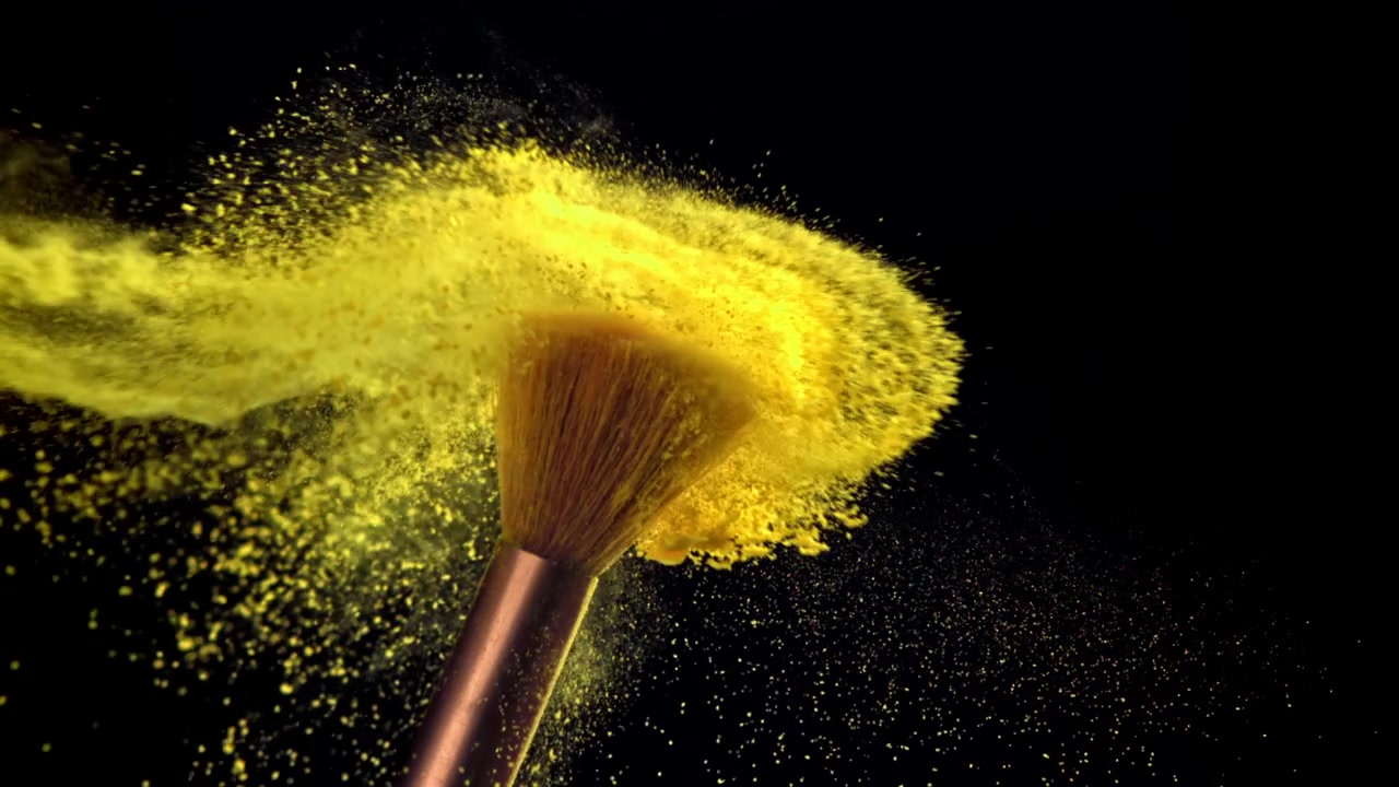 Colisión en cámara lenta de brochas de maquillaje liberando polvo amarillo