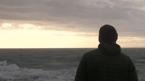 silhouet van een trieste man met uitzicht op ruwe zee bij zonsondergang