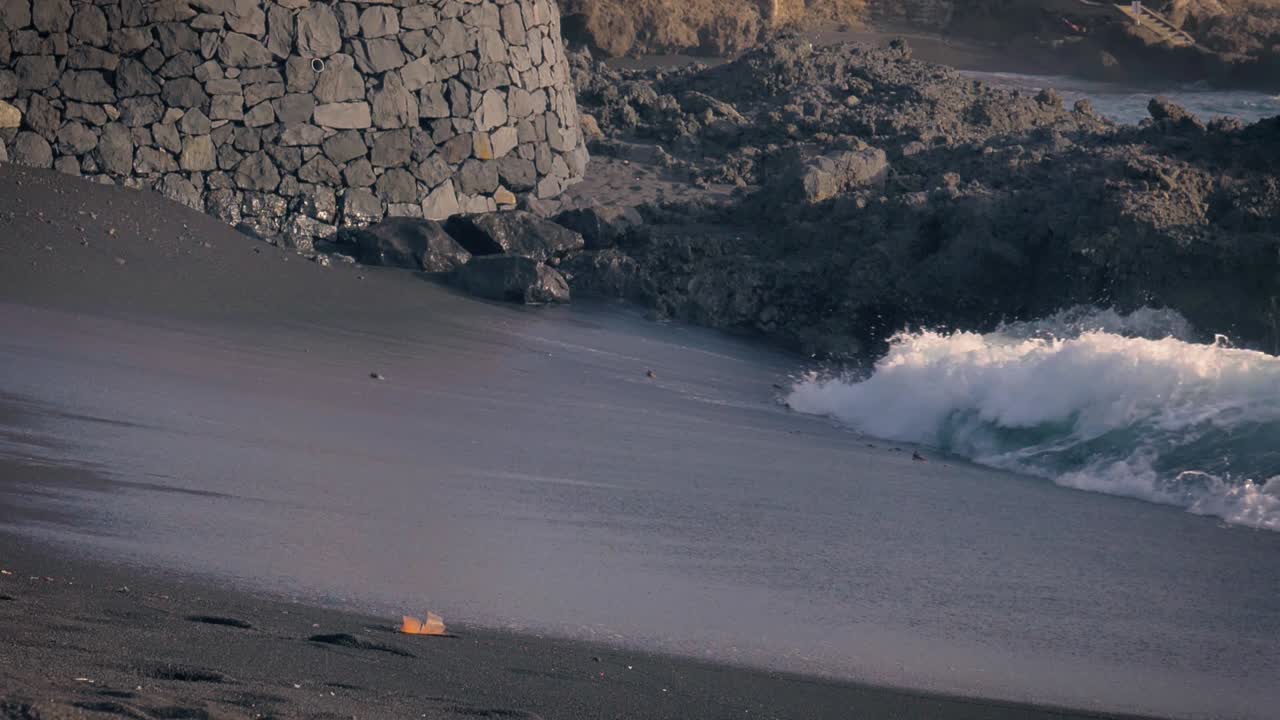 Bellissima spiaggia di sabbia nera di Tenerife con onde che si infrangono sulla riva al rallentatore.