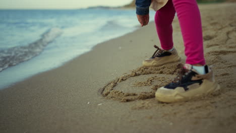 kid standing sand beach at sea nature. little girl legs sneakers play outdoors.