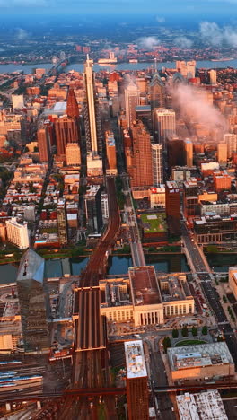 Rays of setting sun lighting the scenery of Philadelphia. Aerial view on the cityscape divided by two rivers. Vertical video
