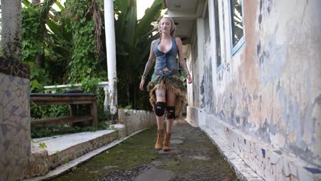 a cool, badass, gypsy looking woman is walking towards the camera on a small path of an abandoned building with jungle and nature on one side in bali