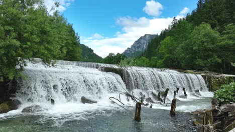Tiro-Estático-De-Las-Cascadas-Naturales-Del-Río-Savinja-En-El-Paisaje-Forestal-Valle-De-Logar-Eslovenia,-Horizonte-Alpino-Durante-El-Verano-Debajo-De-La-Ciudad-De-Luce