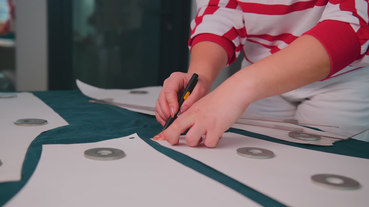 Person marks patterns on fabric pieces with precision. They wear a striped shirt while working. The fabric has circular metal accents. This footage suits fashion design, tailoring, or craft projects
