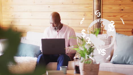 animation of currency symbol and globe over african american man using laptop