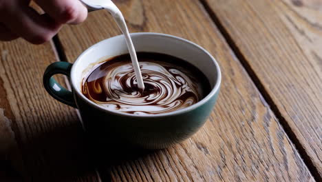 pouring milk into a mug of coffee on a wooden table