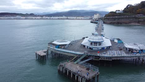 Llandudno-pier-historic-Victorian-wooden-boardwalk-seaside-landmark-aerial-view-orbiting-right-shot-low