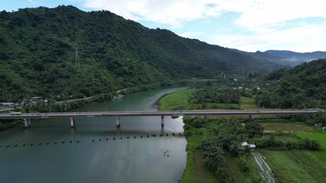 Atemberaubende-Luftaufnahme-Einer-Belebten-Brücke,-Die-Einen-Riesigen,-Malerischen-Fluss-Mit-üppigen-Regenwäldern-Und-Hügeln-Im-Hintergrund-überquert