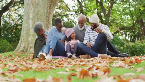 Video-of-happy-african-american-parents-and-daughter-sitting-with-grandparents-in-autumn-garden