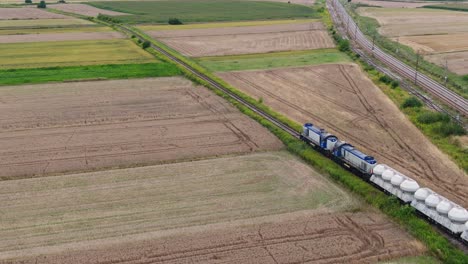 locomotives with freight wagons move through wheat fields, transport train aerial view