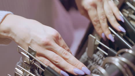 high angle view of manicured nails of woman browsing through shorts rack in modern store feeling fabric texture and assessing style under warm lighting with organized display of casual apparel